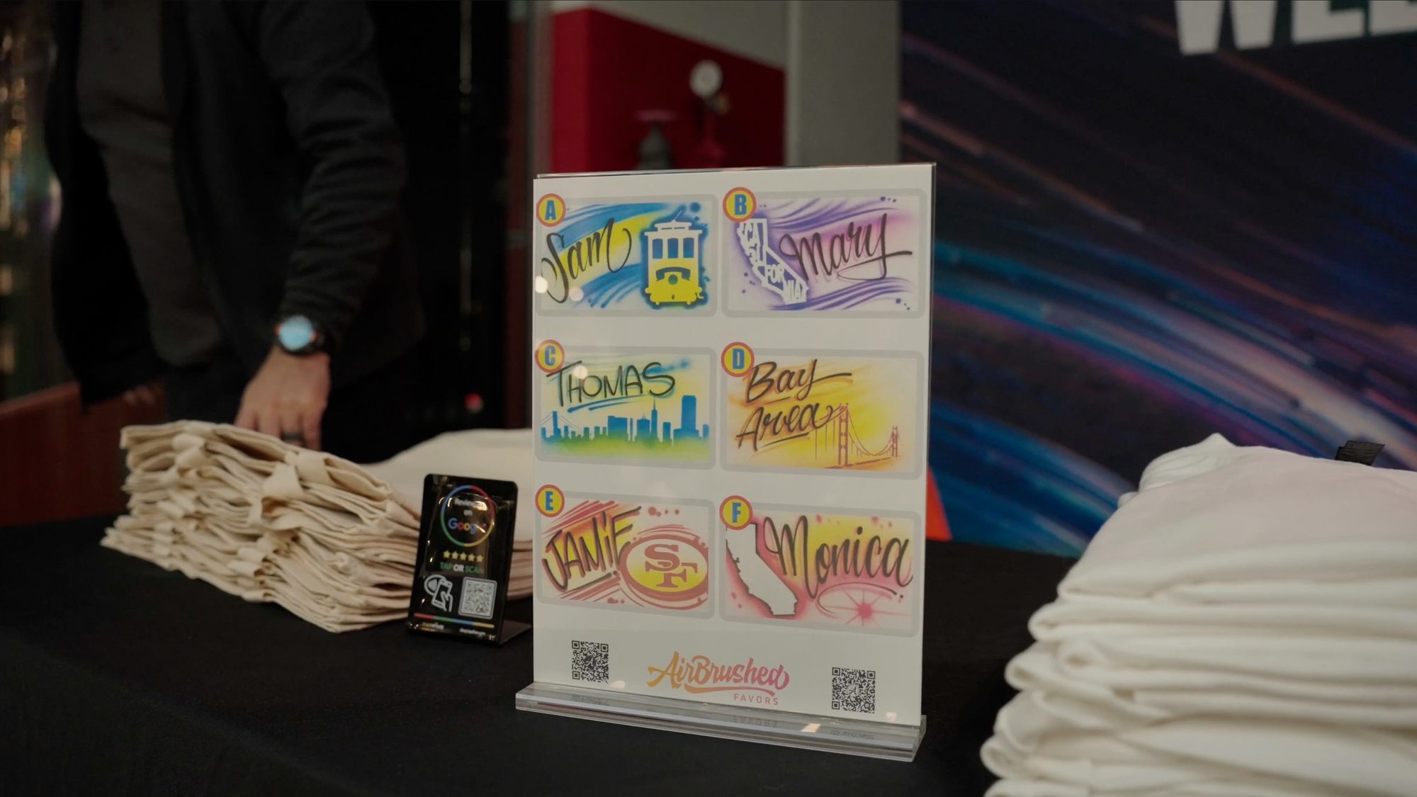Airbrushed shirt designs displayed beside stacks of blank shirts